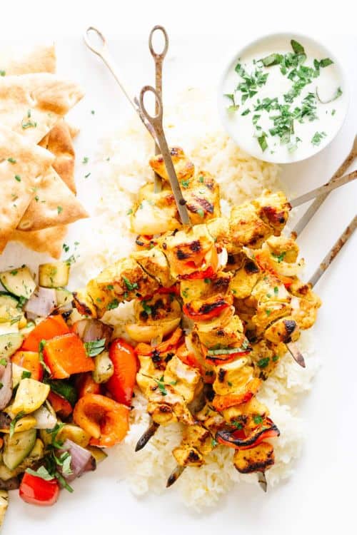 Grilled Tandoori Chicken Kebabs on a white plate with dipping sauce and vegetables