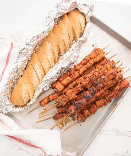 Puerto Rican Grilled Pork Kebabs on a basking sheet with a loaf of bread